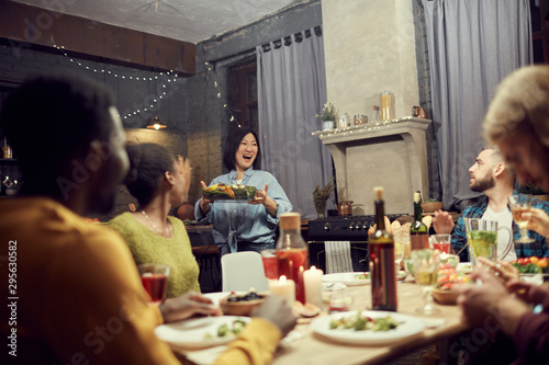 Portrait of excited Asian woman bringing main dish to dinner table during house party with friends, copy space