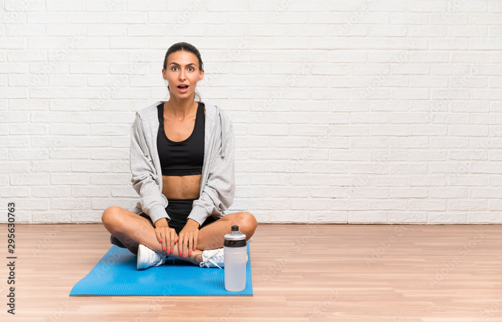 Fototapeta premium Young sport woman sitting on the floor with mat with surprise facial expression