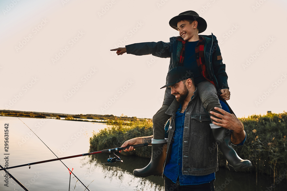 Father and son have fun while fishing. Teen boy happy and smile, sit on  father shoulders and shows hand on float Stock Photo