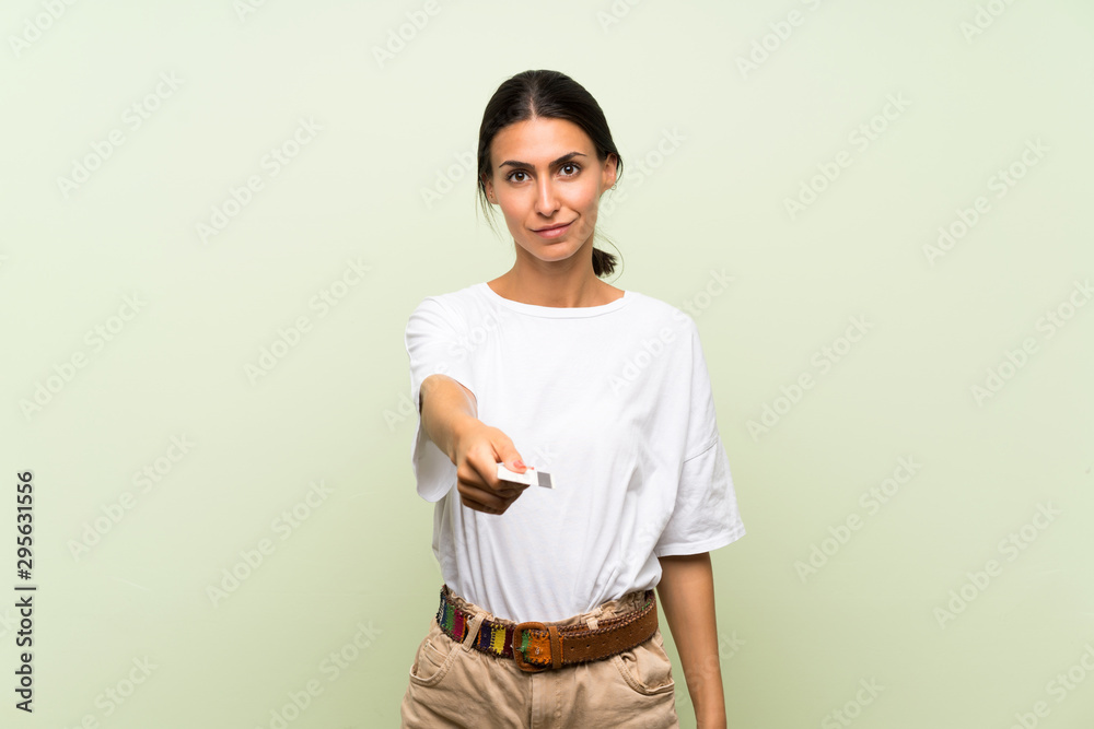 Young woman over isolated green background holding a credit card Young woman over isolated green background holding a credit card
