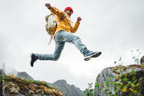 Active brave tourist jumping through cliff in mountain lifestyle outdoor journey. Man traveler with rucksack hiking mountains wilderness