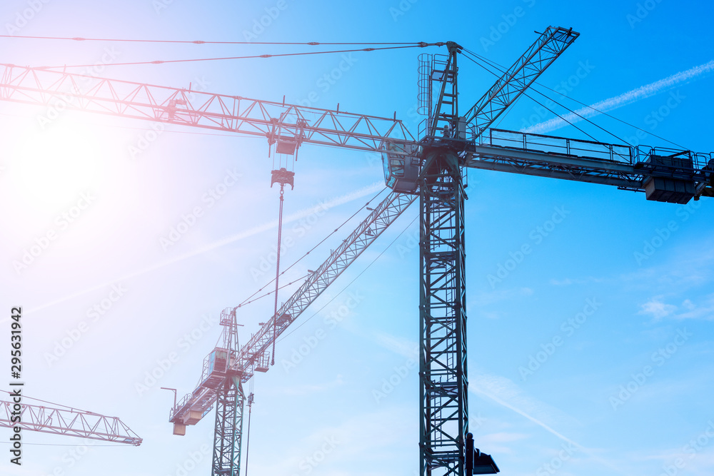 Big tower cranes against the blue sky. Background image of construction equipment close-up with copy space. Big tower cranes against the blue sky. Background image of construction equipment close-up with copy space.
