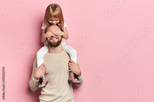 little daughter covering her dad's eyes with a palm. girl having fun with dad. happiness, close up portrait, isolated pink background, copy space photo