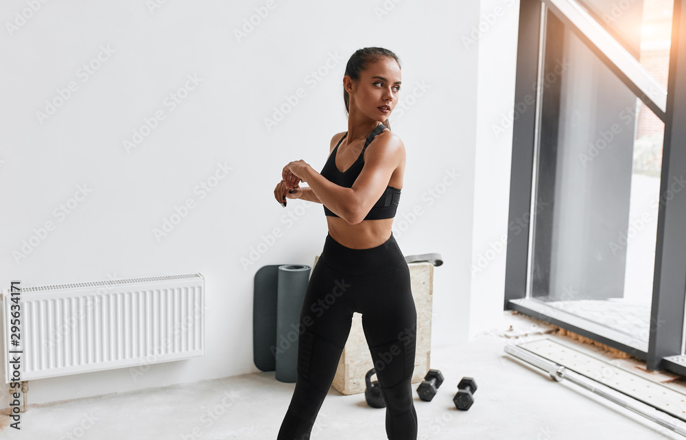 Obraz premium Slim fitness female in black leggins and topic stretching body, arms. White gym background