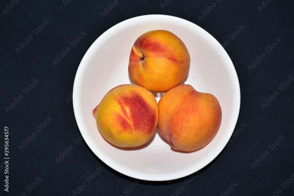 Isolated closeup of 3 three ripe peaches in a white bowl on a black background Isolated closeup of 3 three ripe peaches in a white bowl on a black background