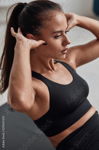Closeup of Long haired fit female in sportswear pumping abdominals sitting on floor in gym. Fitness, sport concept