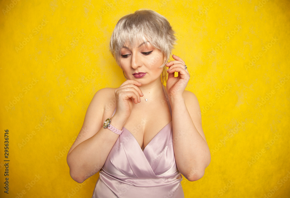 happy short hair blond girl with plus size body posing in lilac color dress on yellow studio background