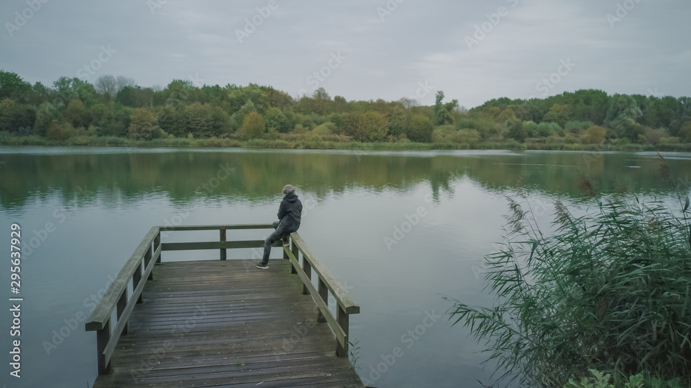 Autumn mood at the lake. Woman with warm clothes on a dock at a lake.Cloudy sky.