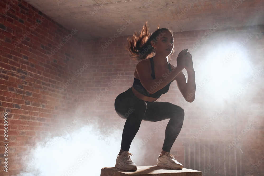 Beautiful sporty woman in sportswear jumping on wooden box in gym. Training, cross fit, sport - obrazy, fototapety, plakaty 