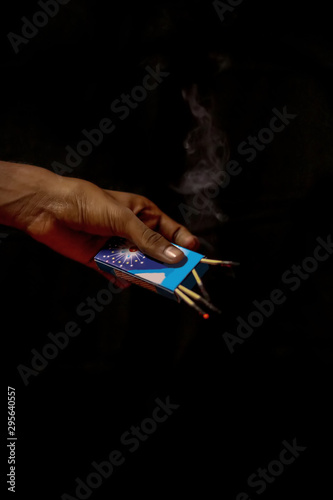 Hand holding an extinguished matchstick on black background.