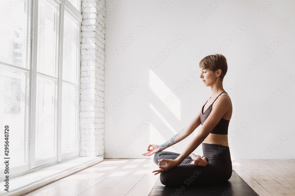 Young woman meditating at class. Beautiful girl practicing yoga at home. Harmony, balance, meditation, relaxation, healthy lifestyle concept - obrazy, fototapety, plakaty 
