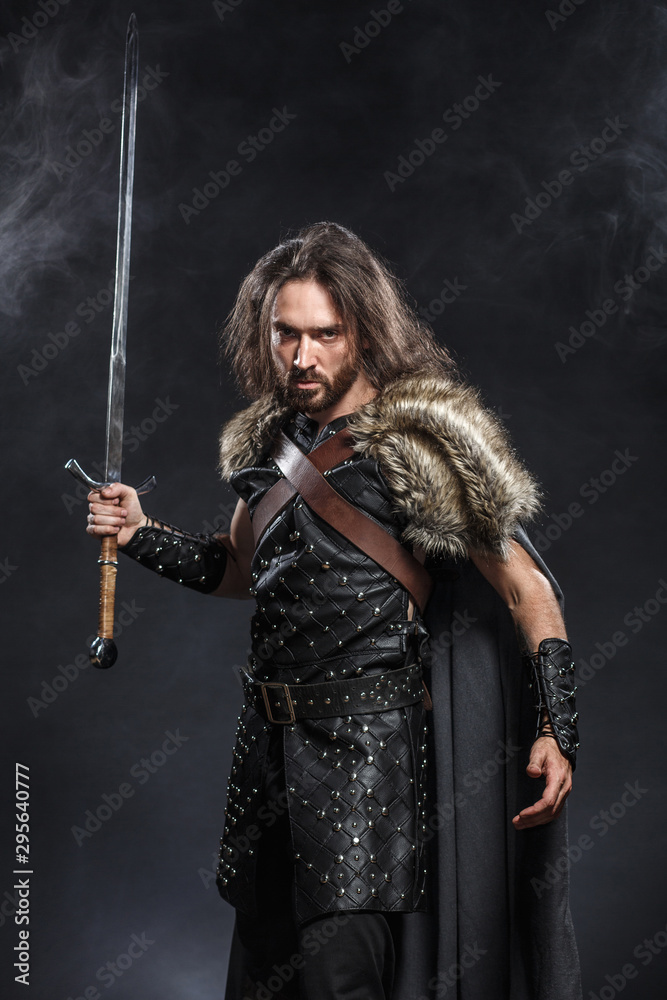 Portrait of a courageous ancient warrior in armor with sword and shield. Concept historical photo of bravery knight with long sword
