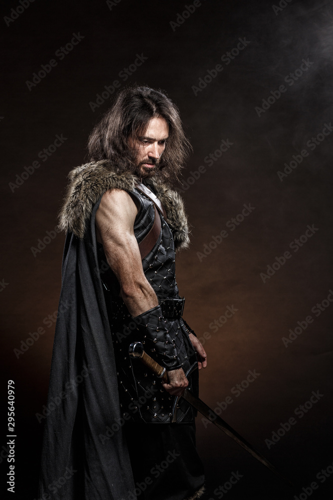 Man dressed in medieval armor and raincoat with longs word fighting against enemy. Courage fantasy warrior knight with long hair concept historical photo Man dressed in medieval armor and raincoat with longs word fighting against enemy. Courage fantasy warrior knight with long hair concept historical photo