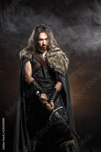 Man dressed in medieval armor and raincoat with longs word fighting against enemy. Courage fantasy warrior knight with long hair concept historical photo