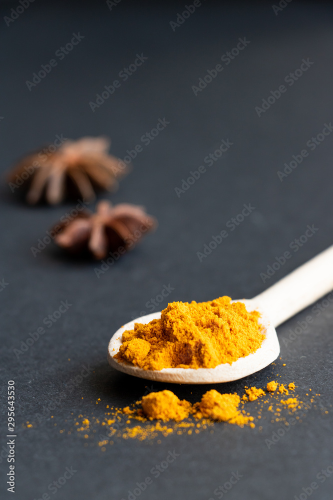 Fototapeta premium Turmeric powder in a wood spoon on a dark background.