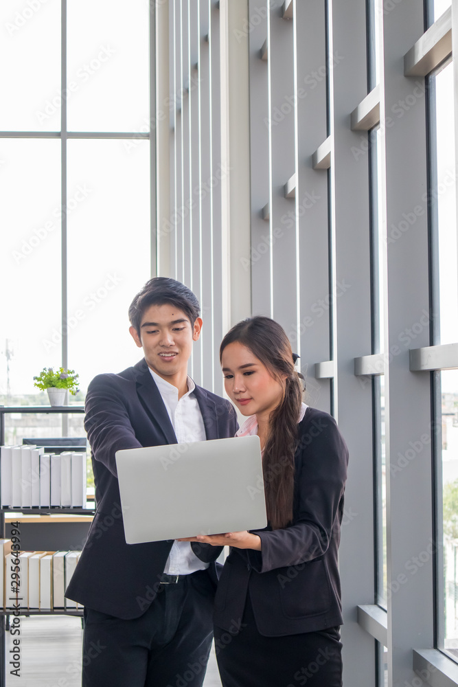 Young Asian businessmen and business women consult the work together. By looking at the notebook in the workplace Young Asian businessmen and business women consult the work together. By looking at the notebook in the workplace