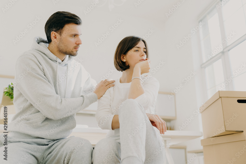 Caring husband tries to calm wife in difficult life situation, relocate in new house for living, pose indoor near carton boxes, solve domestic problems together. Woman in stress, faces trouble Caring husband tries to calm wife in difficult life situation, relocate in new house for living, pose indoor near carton boxes, solve domestic problems together. Woman in stress, faces trouble