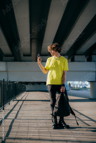 Curly guy with rucksack and smartphone in streen stock photo photo