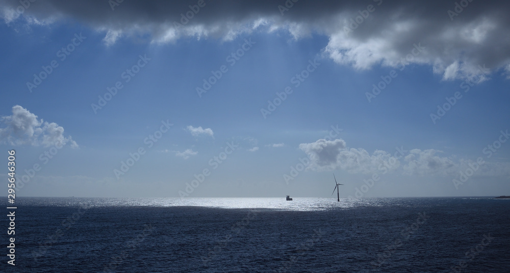 Seascape, wind turbine in the distance on the sea, blue sky and clouds