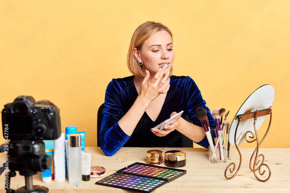 Successful popular young fashion blogger girl sharing makeup hacks with followers, applying eyeshades on lips for rich colour, recording new podcast for personal beauty blog.