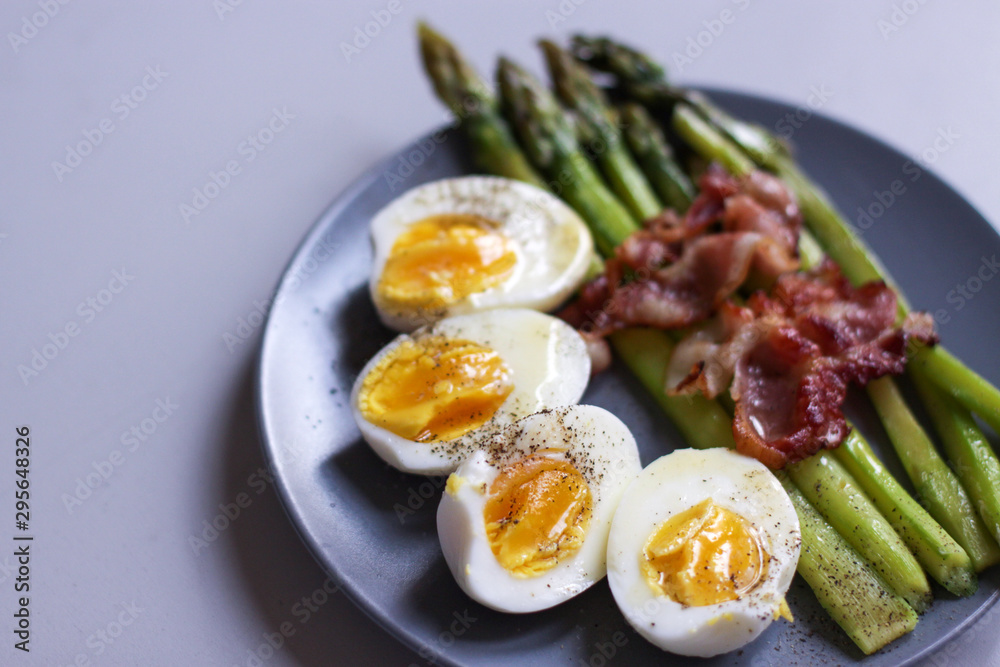 Healthy breakfast - green asparagus wrapped with bacon, boiled egg. Breakfast on a blue table closeup.