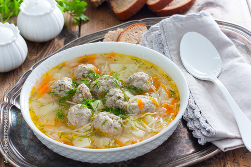 Homemade soup with meatballs and noodles in a white plate on a metal tray, selective focus