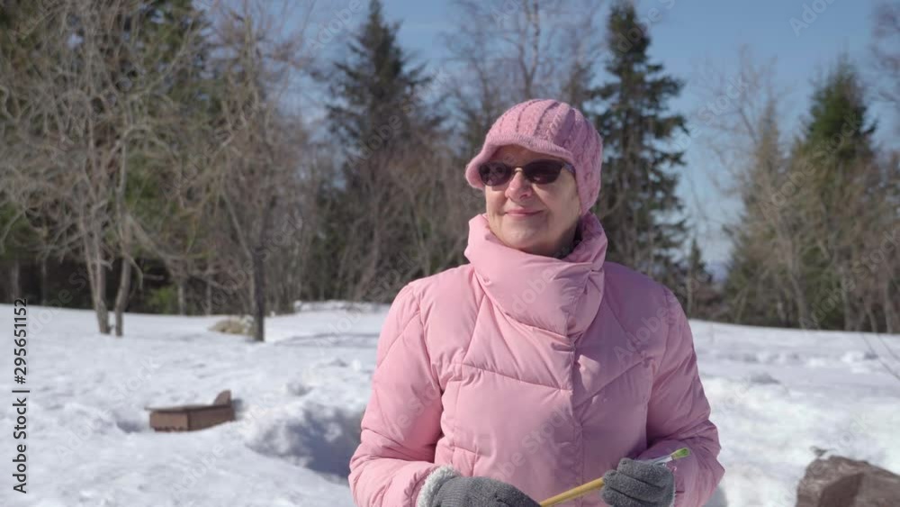close-up. Portrait of an elderly woman tourist exploring winter nature. A bird is jumping in the background.