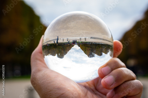 Crystal ball used as telling object. Sperical transparant glass. Paris park in the background with fall or autumn trees color