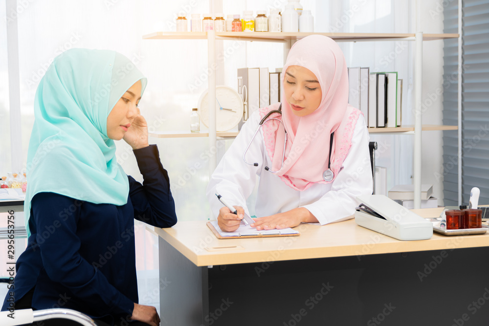 Obraz premium Muslim woman doctor wearing pink muslim headscarf giving advice to a female patient muslim wearing green muslim headscarf at of a doctor's consulting room .