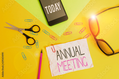 Conceptual hand writing showing Annual Meeting. Concept meaning yearly meeting of the general membership of an organization Paper sheets smartphone scissors eyeglasses colored background photo