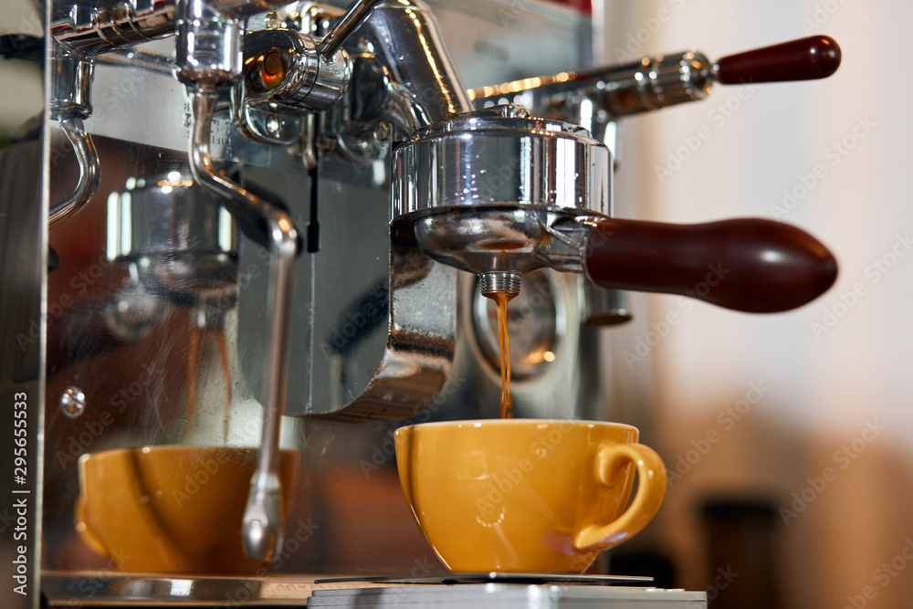 Process of coffee pouring from professional grinder into big yellow cup, blurred background, close up