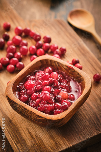 Cranberry jam in a wooden bowl on a wooden background.
