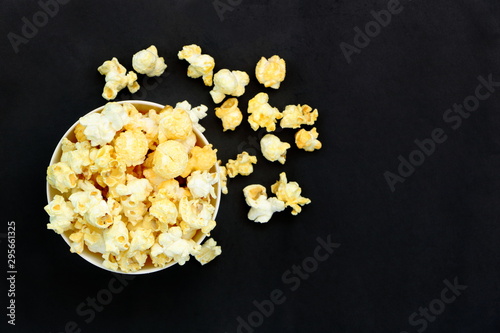 Top view isolated salted popcorn mix with cheese popcorn spilled from white bowl on black table background, movie cinema time concept, have copyspace