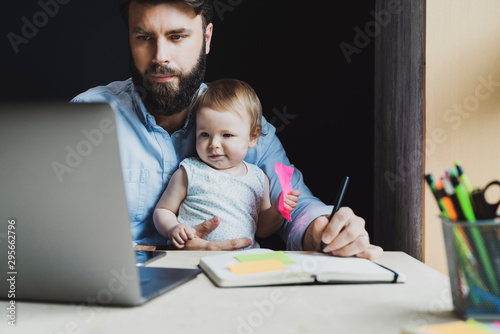 Parent with child studying remotely at homebased laptop. Distant education for people with babies.Man and toddler sitting at table