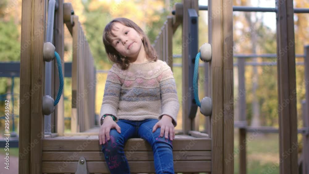 Little cheerful girl playing and fooling around on playground in the autumn city park, slow motion shot. Little cheerful girl playing and fooling around on playground in the autumn city park, slow motion shot.