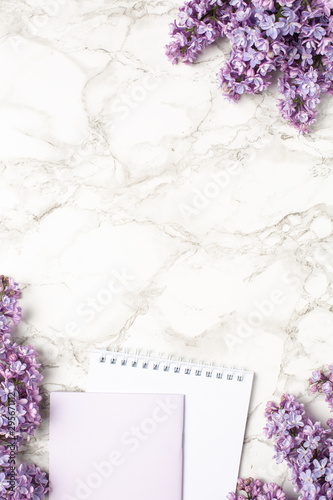 Notebook and purple lilac flowers on marble background  simple business composition with spring flower