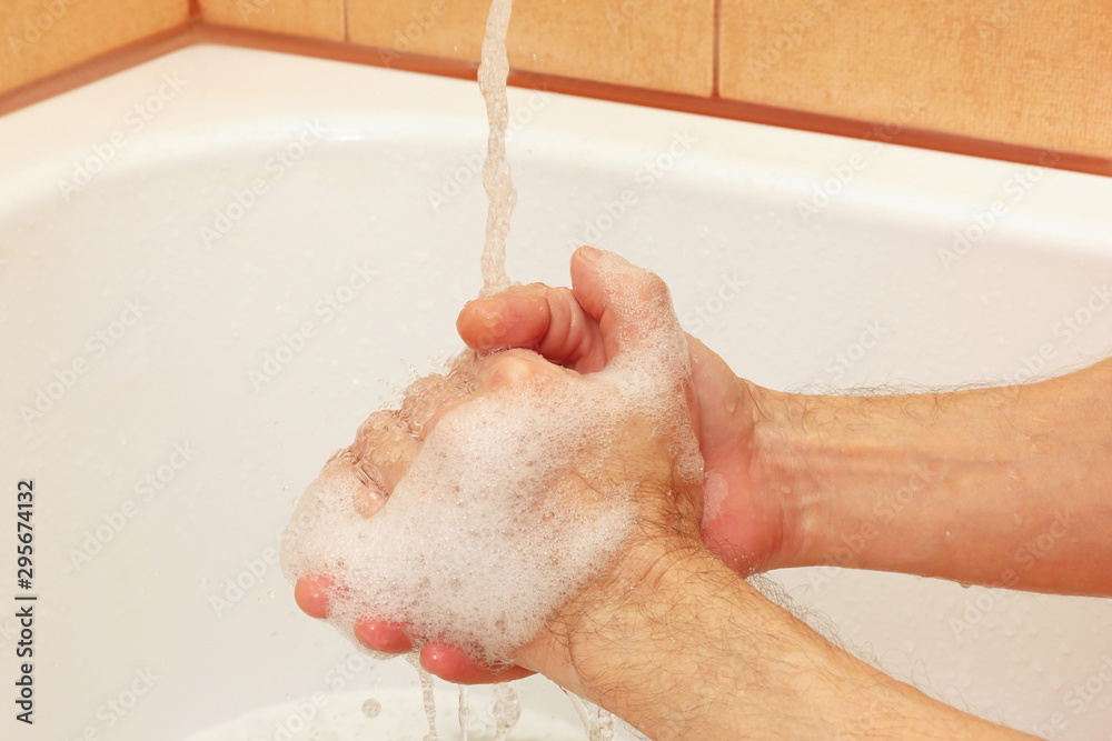 Man`s hands with soap under the jet of water in the bathroom Man`s hands with soap under the jet of water in the bathroom