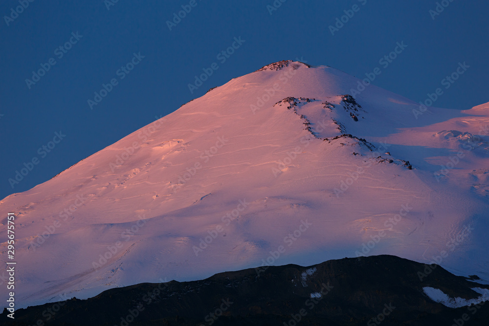 Dawn over the eastern peak of Mount Elbrus. The snow-covered peaks of a stratovolcano are lit by the rays of the rising sun in the North Caucasus in Russia.