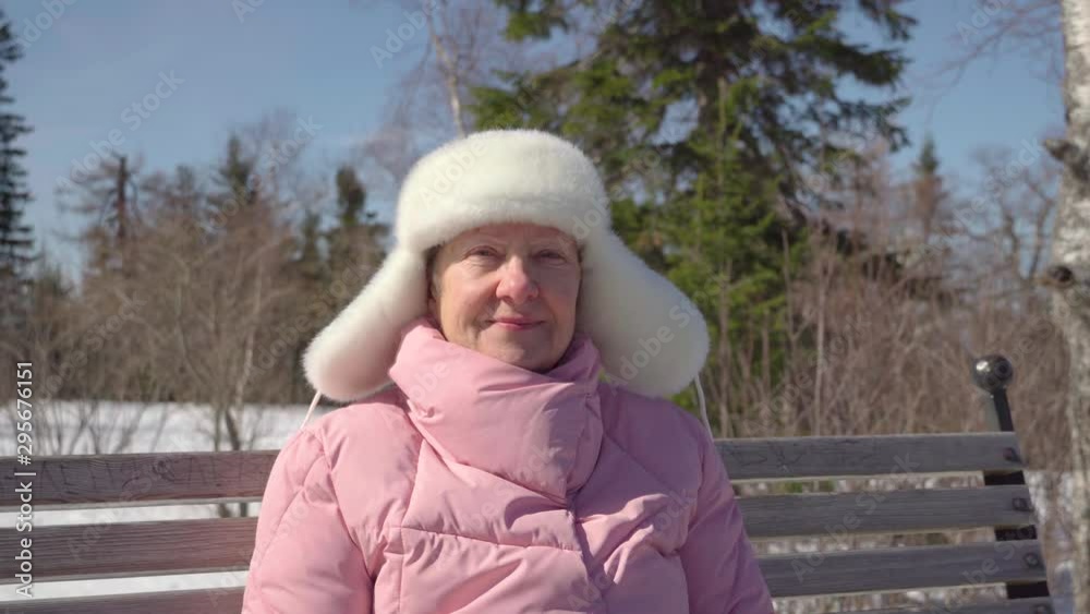 Close-up portrait of an elderly lady outdoors in winter. Grandmother is sitting on a bench and resting.