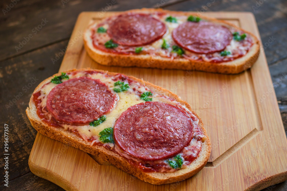 open sandwiches with salami sausage cheese tomato sauce pepperoni pizza style on wooden board close up open sandwiches with salami sausage cheese tomato sauce pepperoni pizza style on wooden board close up