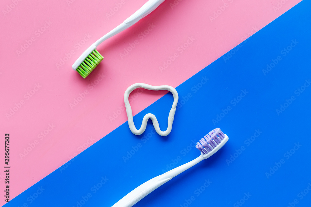 Teeth brushing concept. Tooth drawn with toothpaste near toothbrushes on pink and blue background top view Teeth brushing concept. Tooth drawn with toothpaste near toothbrushes on pink and blue background top view