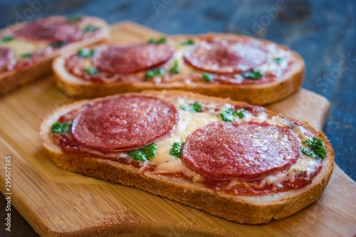 hot open sandwiches with salami cheese tomato sauce pepperoni pizza style on wooden board close up