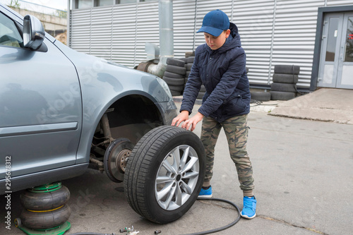 A teenager is changing a wheel on a car. Car on maintenance, repair service.