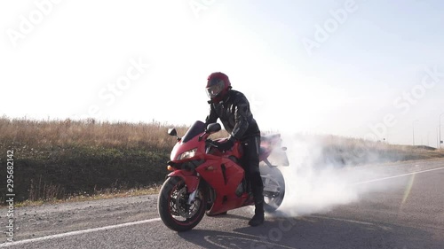 A man in sports equipment and a helmet makes beautiful smoke from under the wheels of a red motorcycle