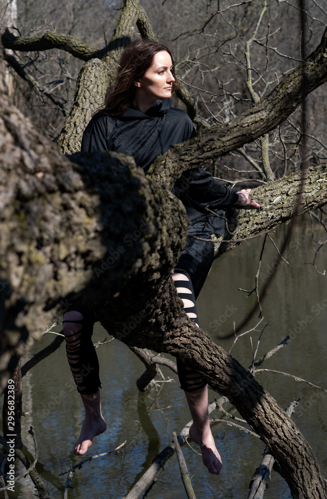 Woman with dark long hair in black robes hanging on tree branches in the middle of a swamp. Halloween and Gothic concept. Witchcraft and magic. Witch. Woman with dark long hair in black robes hanging on tree branches in the middle of a swamp. Halloween and Gothic concept. Witchcraft and magic. Witch.