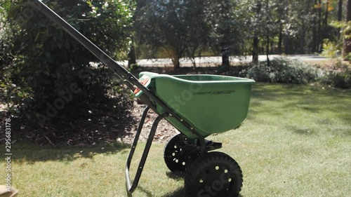 Man fertilizing and seeding residential backyard lawn with manual grass fertilizer spreader. photo