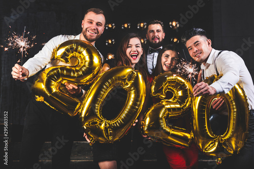 Beautiful young people at a corporate party holding balloons 2020. Happy New Year celebration. Club party with friends