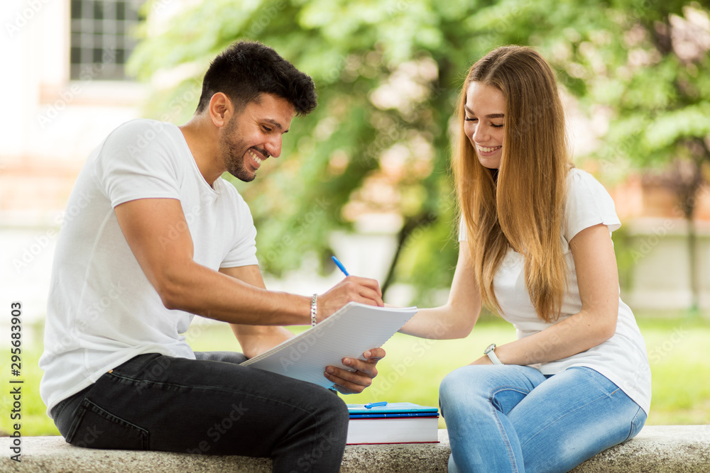 Two students studying together sitting on a bench outdoor Two students studying together sitting on a bench outdoor