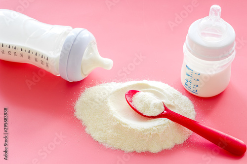 Baby food. Powder in spoon near baby bottle on pink background