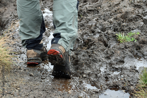 Close up of man's hiking boots and lower trousers, hiking through mud outdoors